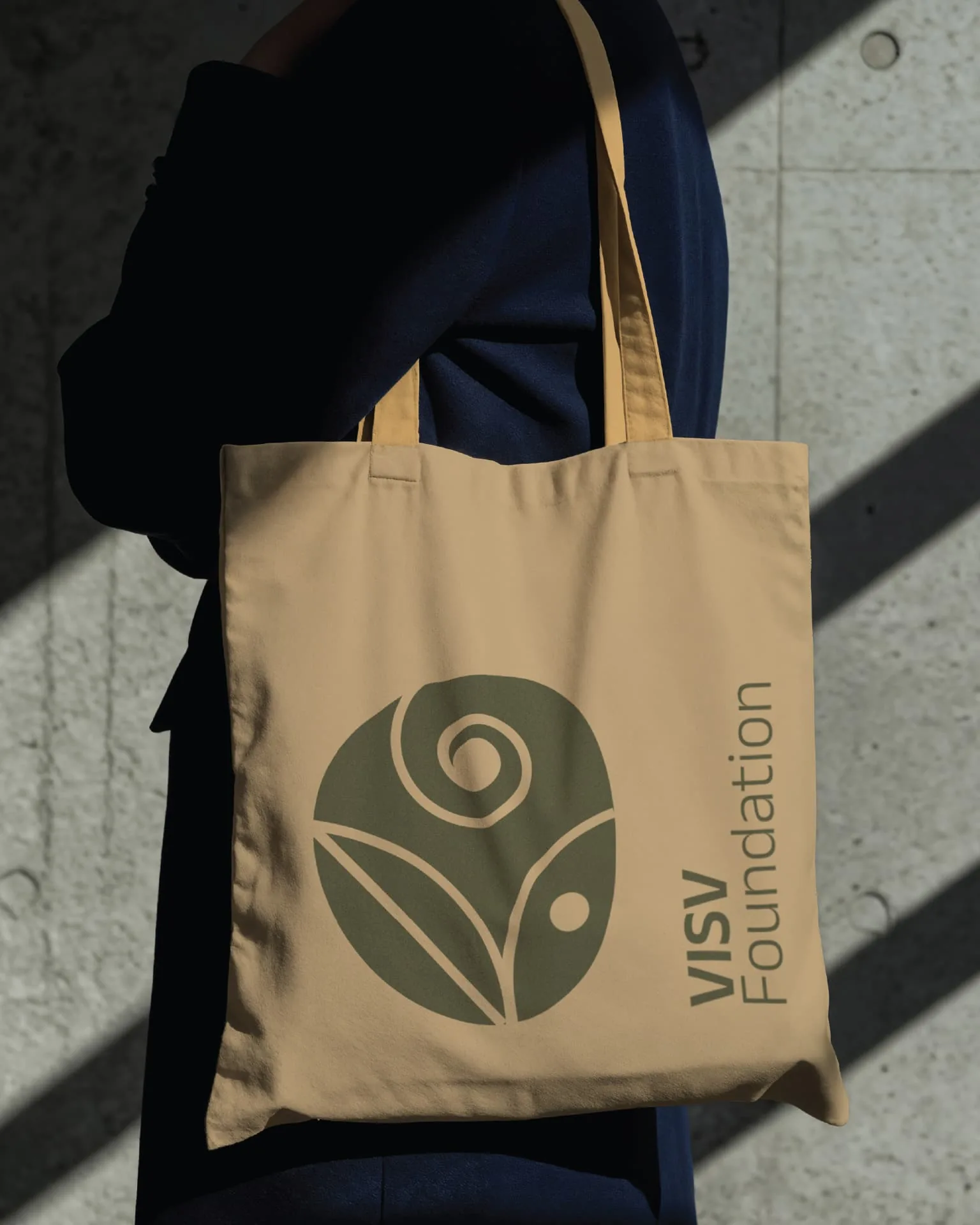 Visv Foundation tote bag — beige canvas bag carried with the green VISV seed emblem printed on it