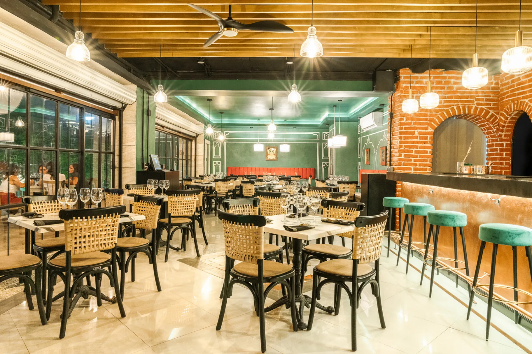 India Jones - Restaurant interior showcasing teal walls, orange brick pizza oven, wicker chairs, and pendant lighting in Playa del Carmen