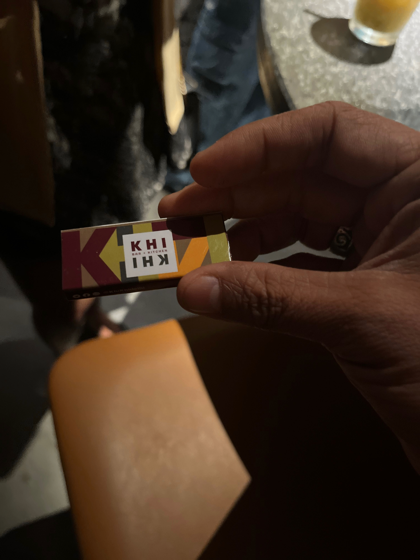 KHI KHI business card being held, featuring colorful geometric pattern and logo design