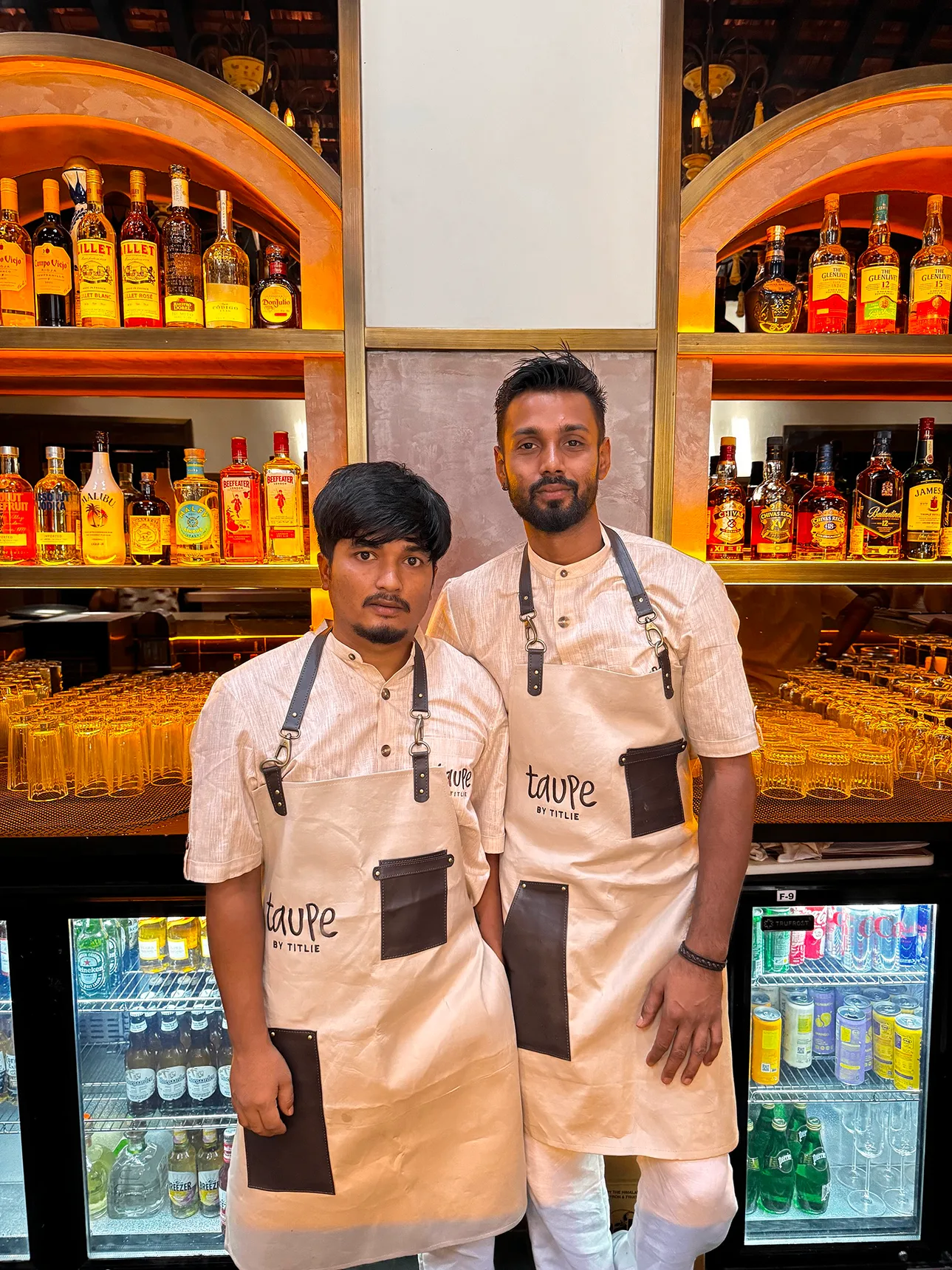 TAUPE restaurant staff members wearing branded aprons behind bar showcasing uniform design and restaurant interior