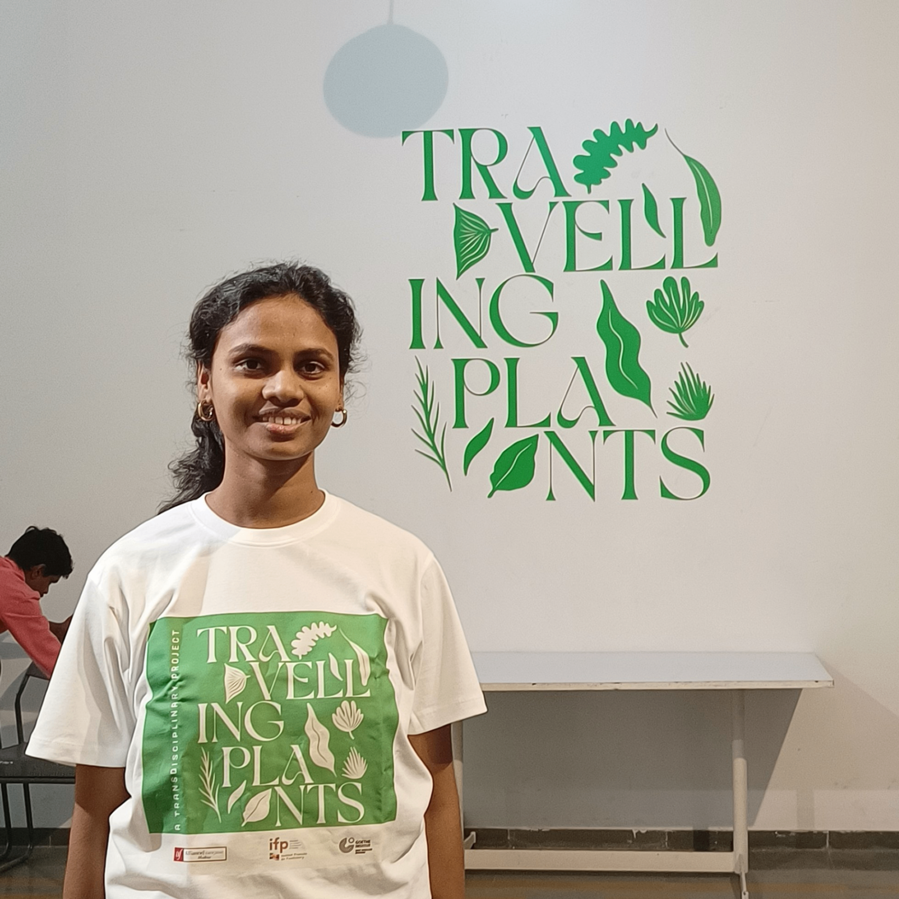 Exhibition visitor wearing Travelling Plants branded t-shirt in front of green botanical wall typography display